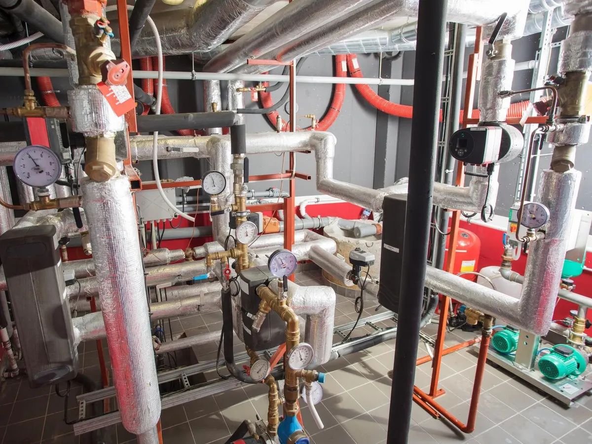 Chaufferie collective avec tuyauteries calorifugées, manomètres et pompes de circulation