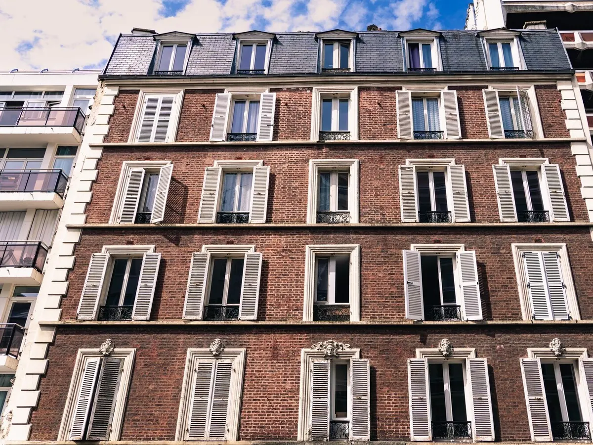 Façade d'un immeuble d'habitation ancien en brique avec volets battants et toiture en ardoise