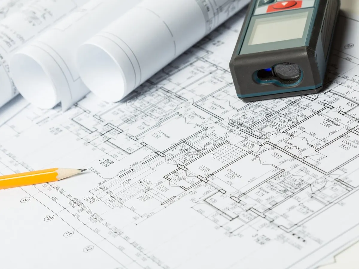 Plans d'étage d'un immeuble d'habitation étalés sur une table avec un télémètre laser et un crayon